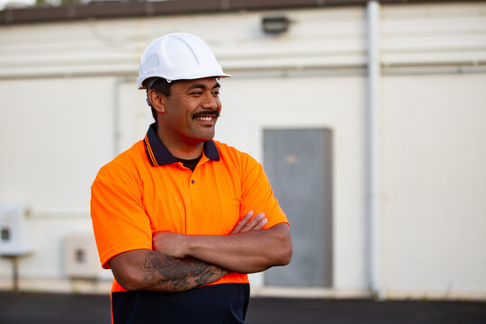 Samoan man wearing hardhat and high visibility clothing standing outdoors with arms crossed