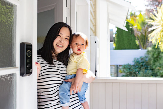 Asian mum standing in porch doorway carrying baby daughter