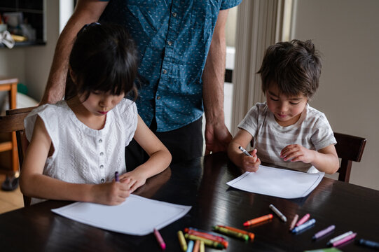 Young children are focused on colouring pictures while sitting at a dining table