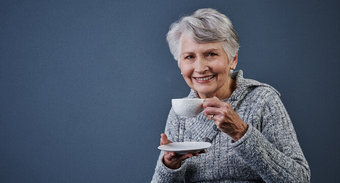 Portrait, space and tea with old woman in studio to relax for break, me time or retirement. Cup, pause and smile with happy senior person drinking beverage on gray background for reset or wellness