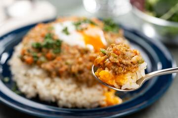 食卓でスプーンで掬ってたべる半熟卵をのせたキーマカレー