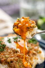 半熟卵をのせたキーマカレーをスプーンで掬って食卓でたべる