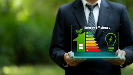 Energy efficiency rating and eco home renovation insulation performance concept. Businessman holding tablet showing a house energy efficiency rating chart. Sustainability and smart home technology. © Antony Weerut