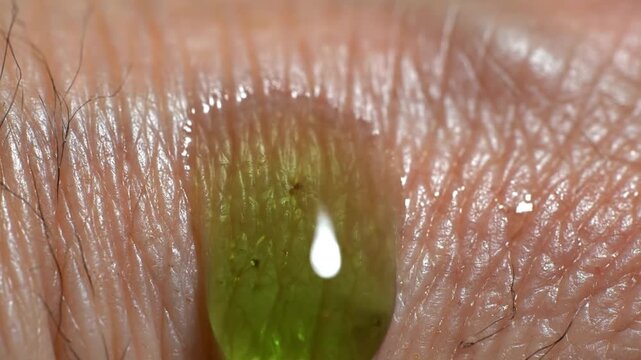 Extreme close-up macro video of a green drop on human skin showing texture, pores, and fine hairs in stunning detail.