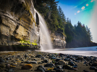 Majestic waterfall cascades onto a rugged pebble beach, captured with a long exposure, showcasing the raw beauty and serene power of Vancouver Island's untamed coastline under a bright sky © Martin
