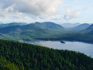 Fototapeta premium Expansive View of Pristine Wilderness on Vancouver Island Dense Evergreen Forests Meet Shimmering Waters of a Secluded Inlet Under an Atmospheric Sky