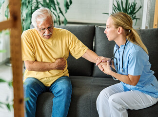 Obraz premium Doctor or nurse caregiver help senior man in pain at home or nursing home