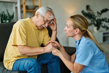 Doctor or nurse caregiver's hand giving support to sad lonely senior man at home or nursing home