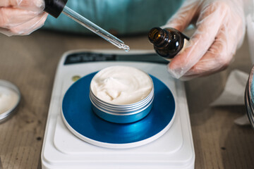 Gloved hands use glass dropper to add liquid to cream jar on digital scale. vegan PDRN, plant nucleotides, DNA repair, elasticity boost.