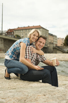 Happy couple hugging while sitting by riverfront with coffee