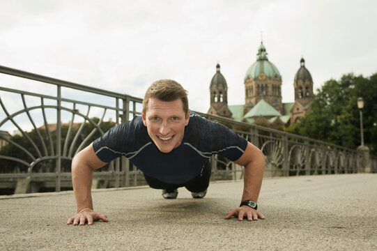 Athletic young man doing push ups on bridge outdoors in city