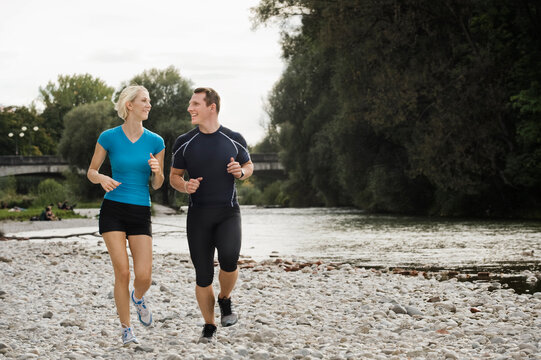 Athletic couple jogging together on rocky riverbank in the city