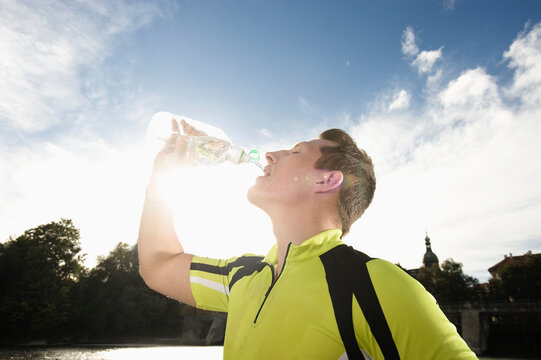 Athletic young man drinking water outdoors after intense workout