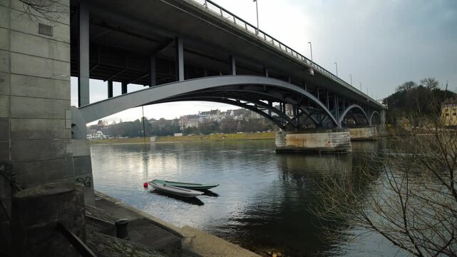 Cinematic pan under the Wettsteinbruecke bridge revealing traditional wooden boats and Basel Minster, Switzerland.