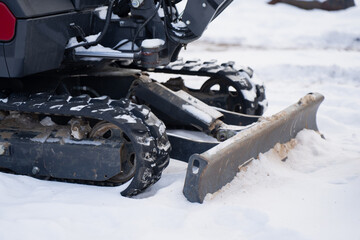 Tracked mini excavator chassis on snow with dozer blade and hydraulic parts, close up of rubber track system, idler wheels and metal plow for cold season worksite operation © K