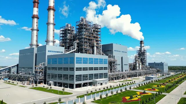 Industrial power plant with smokestacks emitting smoke, surrounded by gardens and greenery, viewed from a distance on a clear day