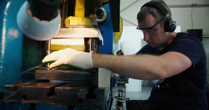 Metal press machine operator working with stamping equipment in factory workshop. Blue-collar manufacturing job