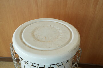 A white bucket with a metal rim sits on a wooden floor. The bucket is empty and has a white lid
