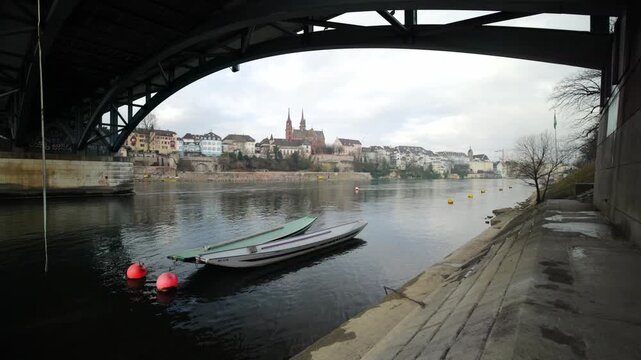 Cinematic pan from under the Wettsteinbruecke bridge revealing traditional boats and the Basel Minster skyline, Switzerland.