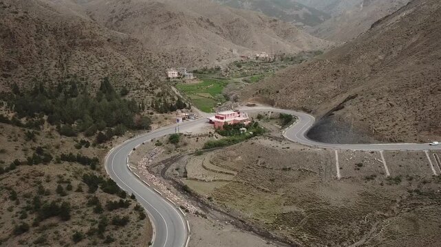 Wide aerial shot capturing a vibrant green oasis with a prominent white building nestled in the rugged, arid landscape of the High Atlas. The footage highlights the stark contrast between fertile pock
