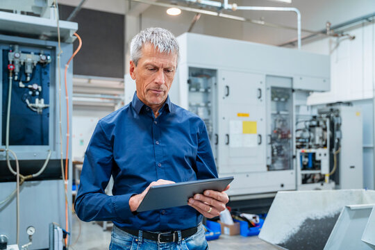 Businessman using tablet PC and standing near machines in factory