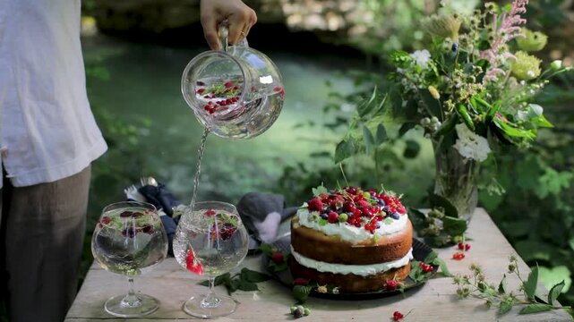 Close up of a server pouring refreshing berry water into glasses at a catered garden party next to a gourmet cake.