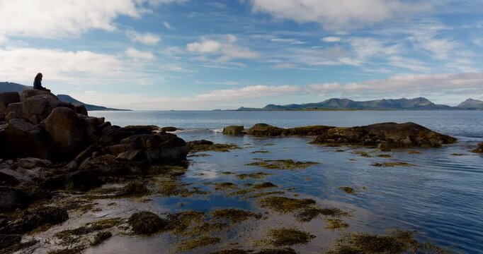 Woman on rocky coast in Stokmarknes, Norway. Serene landscape for mindfulness and wellness content. Aerial drone at low altitude
