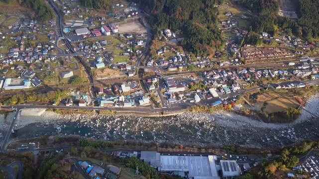 Flyover sunny Nagiso town by shallow river on Kiso Valley floor, Japan