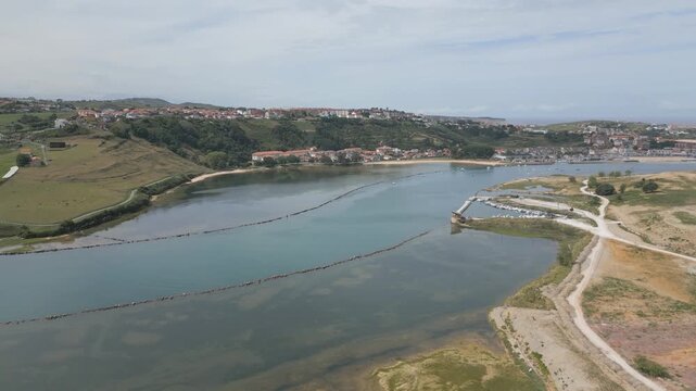 Frontal drone flight over the Suances estuary, revealing the coastal area and the upper part of the town. The shot shows vivid blue inner waters, shoreline and the urban landscape of Suances