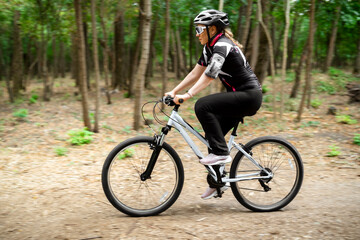 Obraz premium Side view of woman athlete riding mountain bike on forest trail. Professional cyclocross training focusing on speed and physical endurance in nature.
