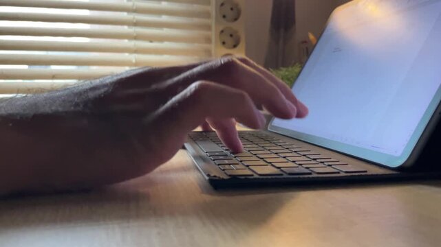 Close up of hands typing on a laptop keyboard with blinds in the background