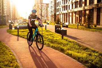 Woman cyclist riding on red bike lane in modern city district during sunset. Regular cardio training for health and energy in urban environment.