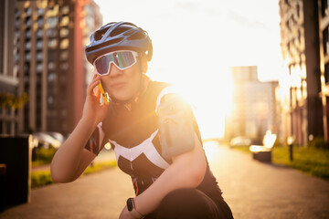 Close up portrait of woman cyclist in helmet talking on mobile phone during golden hour. Connection and safety in modern city environment.