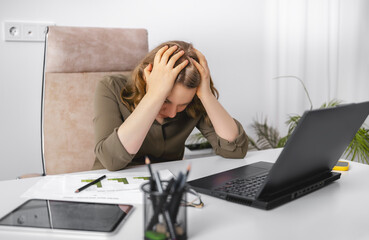 Stressed woman holding head in hands sitting at office desk with laptop and financial reports. Emotional burnout, professional failure, extreme deadline pressure, work crisis despair.