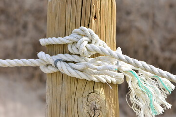 White synthetic rope tied around weathered wooden post forming fence to protect coastal dunes during regeneration process. Location: Tawharanui Peninsula New Zealand