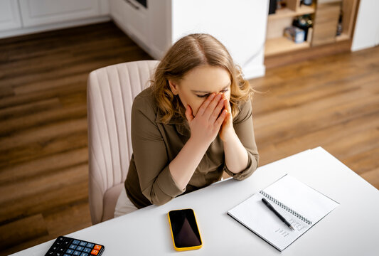 Distressed woman covering face with hands sitting at desk with notebook. Personal financial crisis, family budget despair, emotional breakdown, money loss anxiety, debt problems.