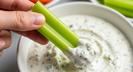 Hand dipping celery into creamy dip.