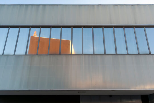 Facciata moderna di un edificio per uffici con facciata esterna in vetro e finestre rettangolari. Design dell'edificio include eleganti telai metallici. Una struttura adiacente si specchia nel vetro