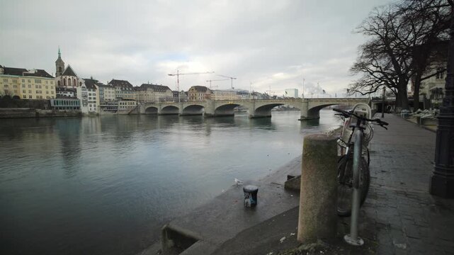 Cinematic pan of the Rhine river promenade with bicycles and the Mittlere Bruecke in Basel, Switzerland.