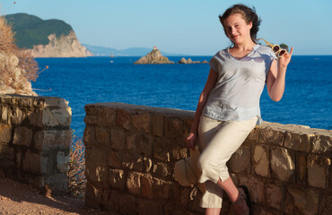 Young female traveler posing with sunglasses by the sea at sunset, summer vacation in Montenegro.