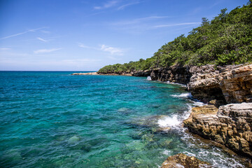 Naklejka premium Scenic view of a rocky coastline with crystal clear turquoise water and green hills 