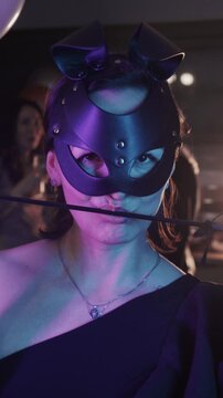 Masquerade party - a woman in a black masquerade mask plays with a camera with a feather tickler