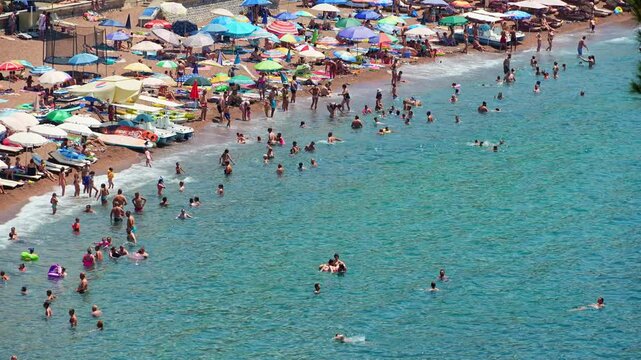 urban beach with sun beds and umbrellas, beach holidays in summer, people swim in the Adriatic Sea in Petrovac, Montenegro
