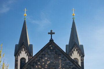 Fototapeta premium Gothic-style church with two tall spires topped with golden crosses against a clear blue sky, showcasing intricate stonework and architectural details