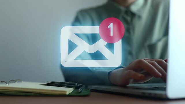 Person checking email on laptop with notification symbol in office setting during late afternoon hours.