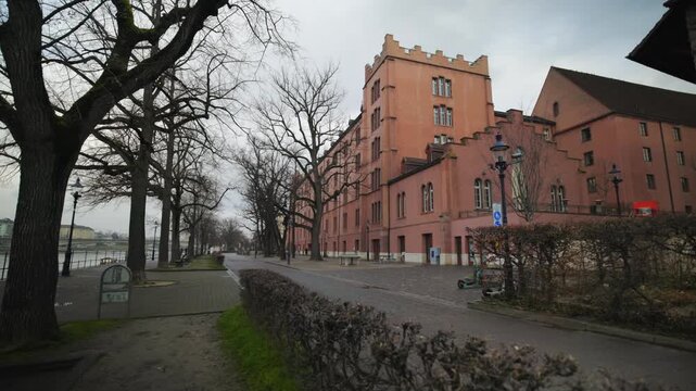 Historical Kaserne building complex with pan and empty riverside walkway in Basel, Switzerland.