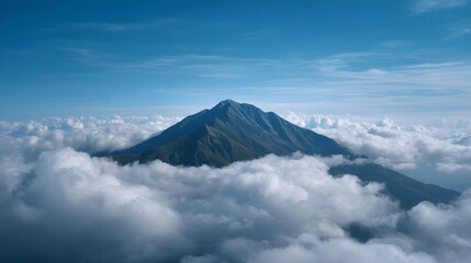Majestic mountain peak emerges from a sea of fluffy white clouds under a clear blue sky