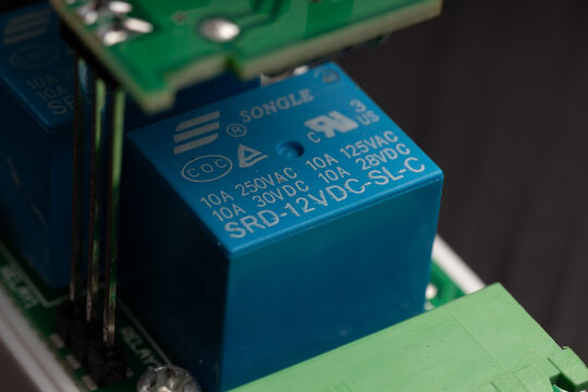 A blue relay with electrical ratings printed on it, part of a green circuit board assembly.