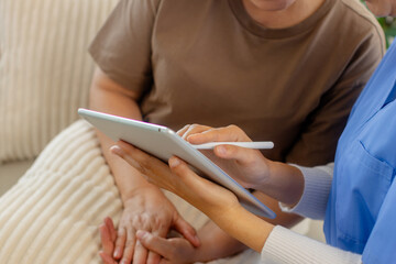 Caregiver reviews a digital checklist on a tablet during consultation, caregiving, care planning, and patient support while sitting on sofa at home. Elderly Care Assistance ,Health Advice Using Tablet © SAT65