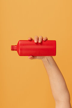 A hand holding a red bottle upside down with cap off